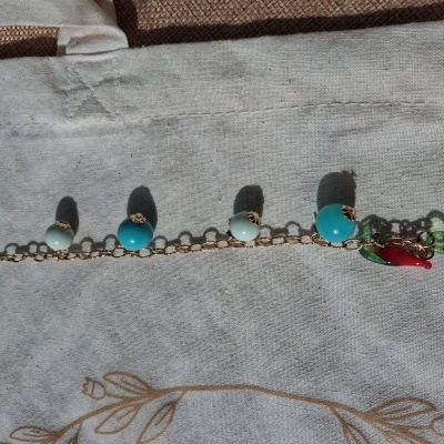 pulseira dourada com esferas azuis e brancas e pendentes de pimento e folhas sobre tecido bege