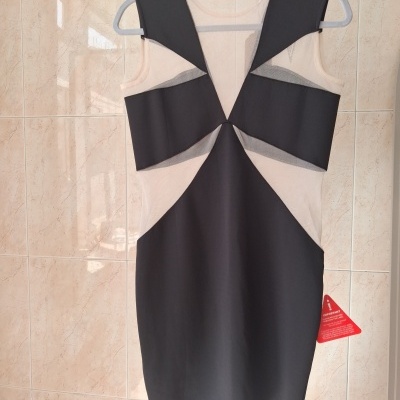 Vestido preto com tecido transparente bege pendurado num cabide cinzento contra parede de azulejos bege