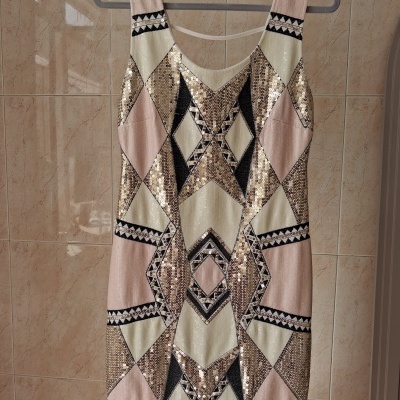 Vestido com padrão geométrico e lantejoulas pendurado num cabide.