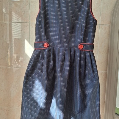 Vestido azul escuro com pontos rosas e botões cor-de-rosa pendurado num cabide cinzento