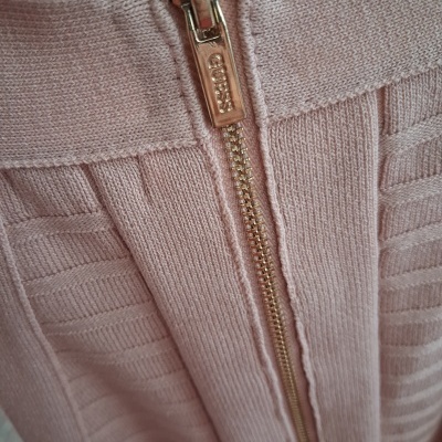 Fecho dourado com GUESS em roupa malha rosa texturada.