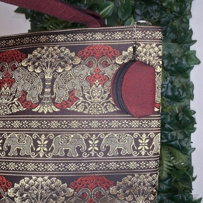 Sacola estampada com elefantes e árvores em dourado, vermelho e preto com alça vermelha e acessório redondo