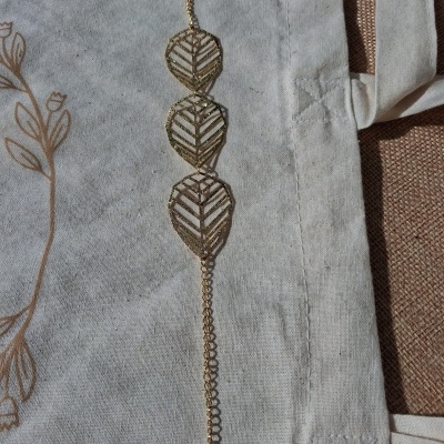 Pulseira dourada com folhas estilizadas sobre tecido claro com padrão floral