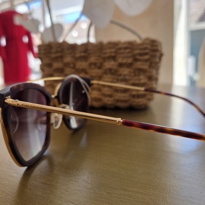 Óculos de sol com armação padrão tartaruga e hastes douradas sobre mesa com cesta ao fundo