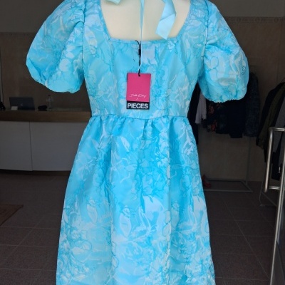 Vestido azul claro com padrão floral, mangas bufantes e laço no pescoço num manequim