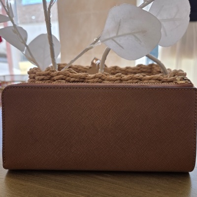 Carteira castanha de pele com textura sobre mesa de madeira e vaso decorativo ao fundo