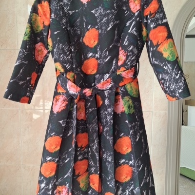 Vestido com padrão floral em tons laranja, verde e rosa sobre fundo preto e cinza