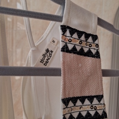 Peça de roupa branca com padrão preto e detalhes com lantejoulas pendurada num cabide cinzento