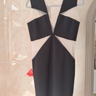 Vestido preto com recortes transparentes em tecido bege claro pendurado num cabide cinzento