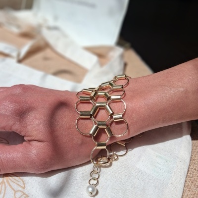 Pulseira dourada com elos hexagonais e pérola no pulso