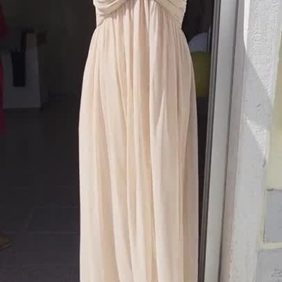 Vestido longo bege claro em manequim à entrada de loja, tecido balançando com o vento.