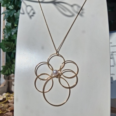 Colar dourado com pendente floral e pérola central num suporte branco