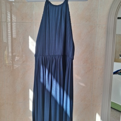 Vestido azul escuro com alças finas em cabide branco sobre parede de azulejo bege
