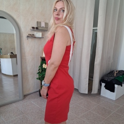 Mulher de vestido justo vermelho com faixa branca ao lado, dentro de sala com cortinas e espelho.