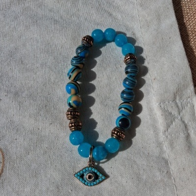 Pulseira azul com contas e pendente em forma de olho sobre tecido bege