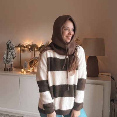 Mulher com camisola de listas castanhas e brancas, capuz castanho e jeans azuis em sala decorada