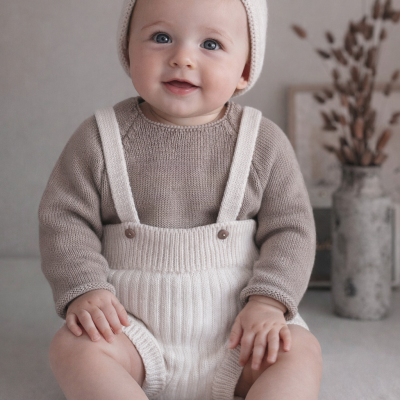 Bebé sentado com roupa de malha bege e creme num ambiente neutro