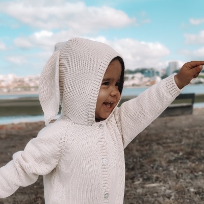 Criança com camisola de malha creme com capuz com orelhas ao ar livre junto a rio