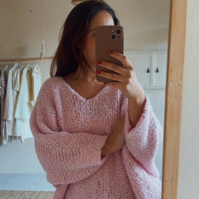 Pessoa com camisola rosa de malha grossa e calças de ganga a tirar selfie no espelho