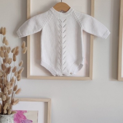 Macacão de malha branco para bebé pendurado numa moldura na parede