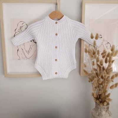 Body de bebé branco com botões pendurado entre quadros com ilustrações e vaso com flores secas