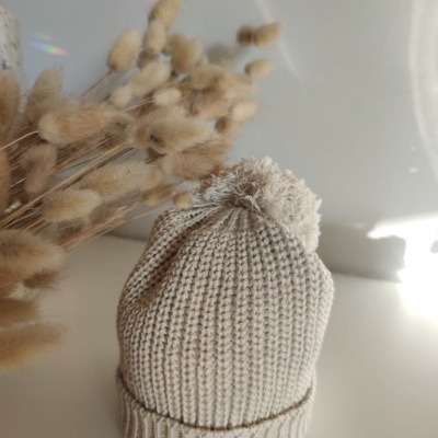 Gorro de malha bege com pompom sobre superfície clara