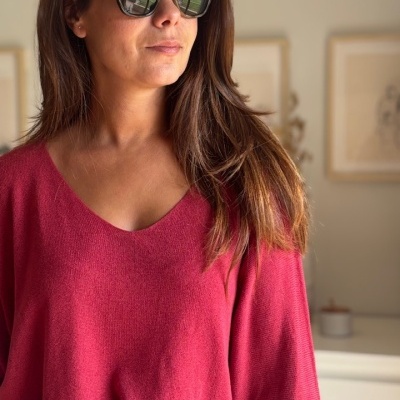 Mulher com suéter vermelho e óculos de sol, interior com quadros ao fundo