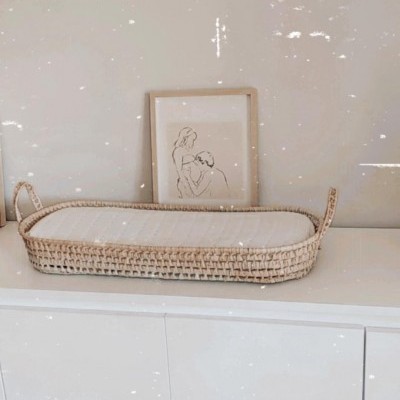 Cesto trançado retangular com alças sobre móvel branco e quadro com desenho minimalista no fundo