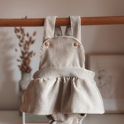 Jardineira de bebé creme com riscas, botões de madeira e saia franzida pendurada numa barra de madeira