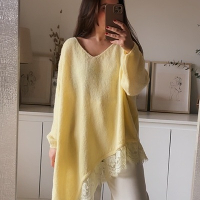 Mulher com camisola amarela de renda e calças brancas perante espelho em sala clara