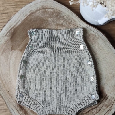 Macacão de bebé cinza claro em malha com botões em tábua de madeira e vaso branco com flores secas