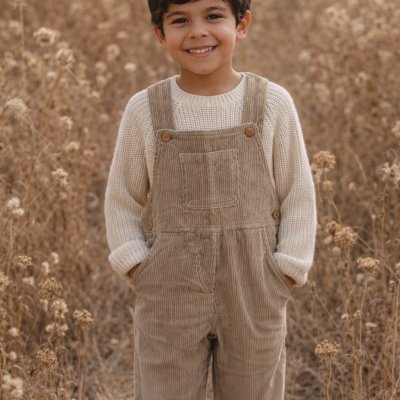 Criança sorridente com macacão castanho e camisola creme em campo seco