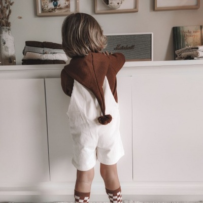 Criança de costas com roupa castanha e branca em ambiente interior