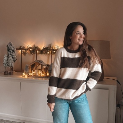 Pessoa com camisola de riscas brancas e castanhas, jeans e sapatilhas em ambiente com decoração natalícia