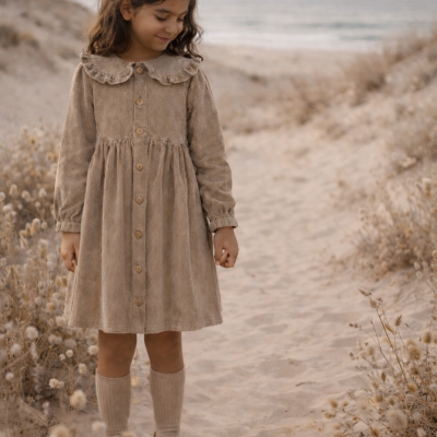 Menina com vestido castanho de veludo cotelê, meias castanhas e sapatos castanhos em caminho de areia