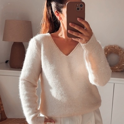 Pessoa a tirar selfie com camisola creme felpuda e calças brancas em interior com móvel branco e candeeiro