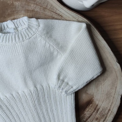 Camisola branca em malha fina sobre tábua de madeira com vaso branco