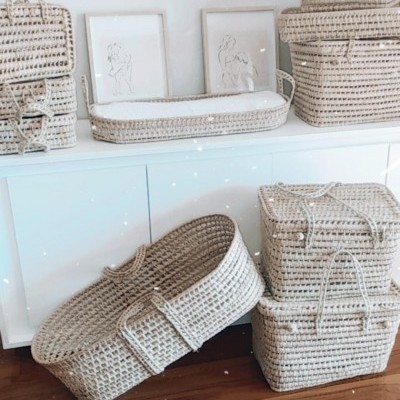 Cestos de vime de vários tamanhos e molduras com desenhos lineares numa sala com móvel branco e chão de madeira.