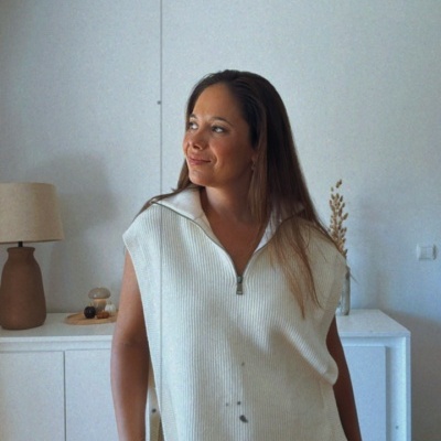 Mulher com camisola branca de malha e calças castanhas em sala interior