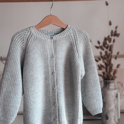 Camisola de malha cinza com botões pendurada em cabide de madeira