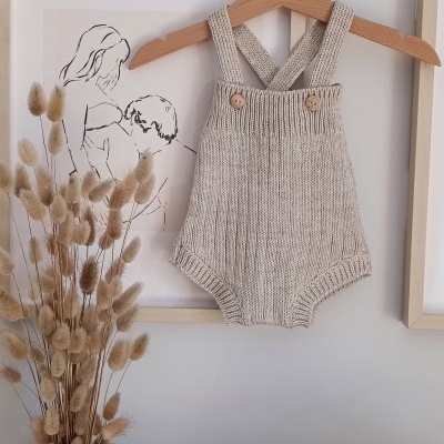 Macacão de bebé cinza claro em malha com alças cruzadas pendurado num cabide de madeira