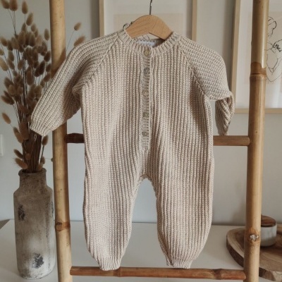 Macacão de bebé bege em malha pendurado em estrutura de bambu