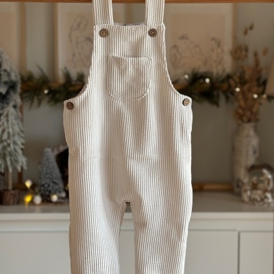 Macacão infantil creme canelado com botões marrons pendurado num cabide de madeira