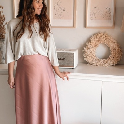 Mulher com camisola branca e saia rosa em ambiente interior com decor minimalista