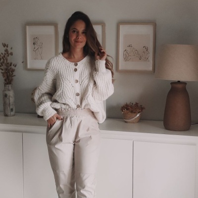 Mulher com casaco branco de malha e calças bege em ambiente interior minimalista