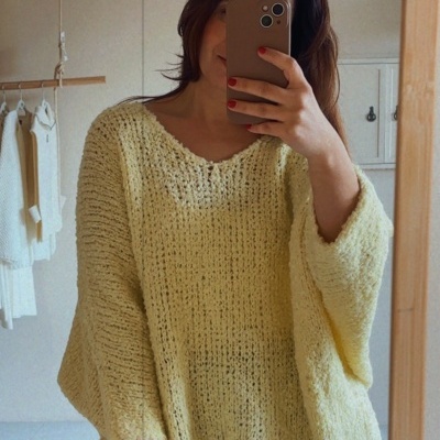 Pessoa com camisola amarela de malha oversized e calças azuis a tirar selfie em espelho