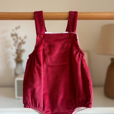 Macacão de bebé vermelho em veludo cotelê com botões, pendurado num cabide de madeira