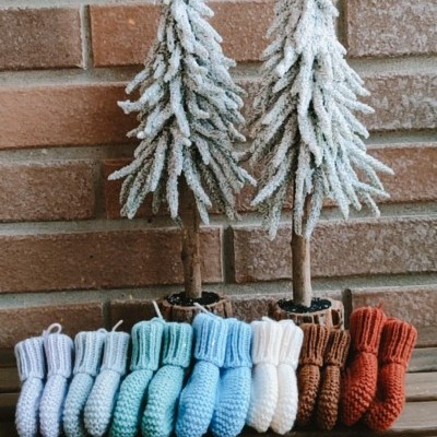 Botas de bebé em crochet coloridas e árvores decorativas com efeito de neve sobre superfície de madeira