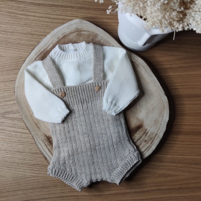 Macacão bege de malha com camisola branca sobre placa de madeira e vaso com flores secas