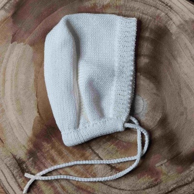 Gorro branco de malha com cordões sobre suporte redondo de madeira